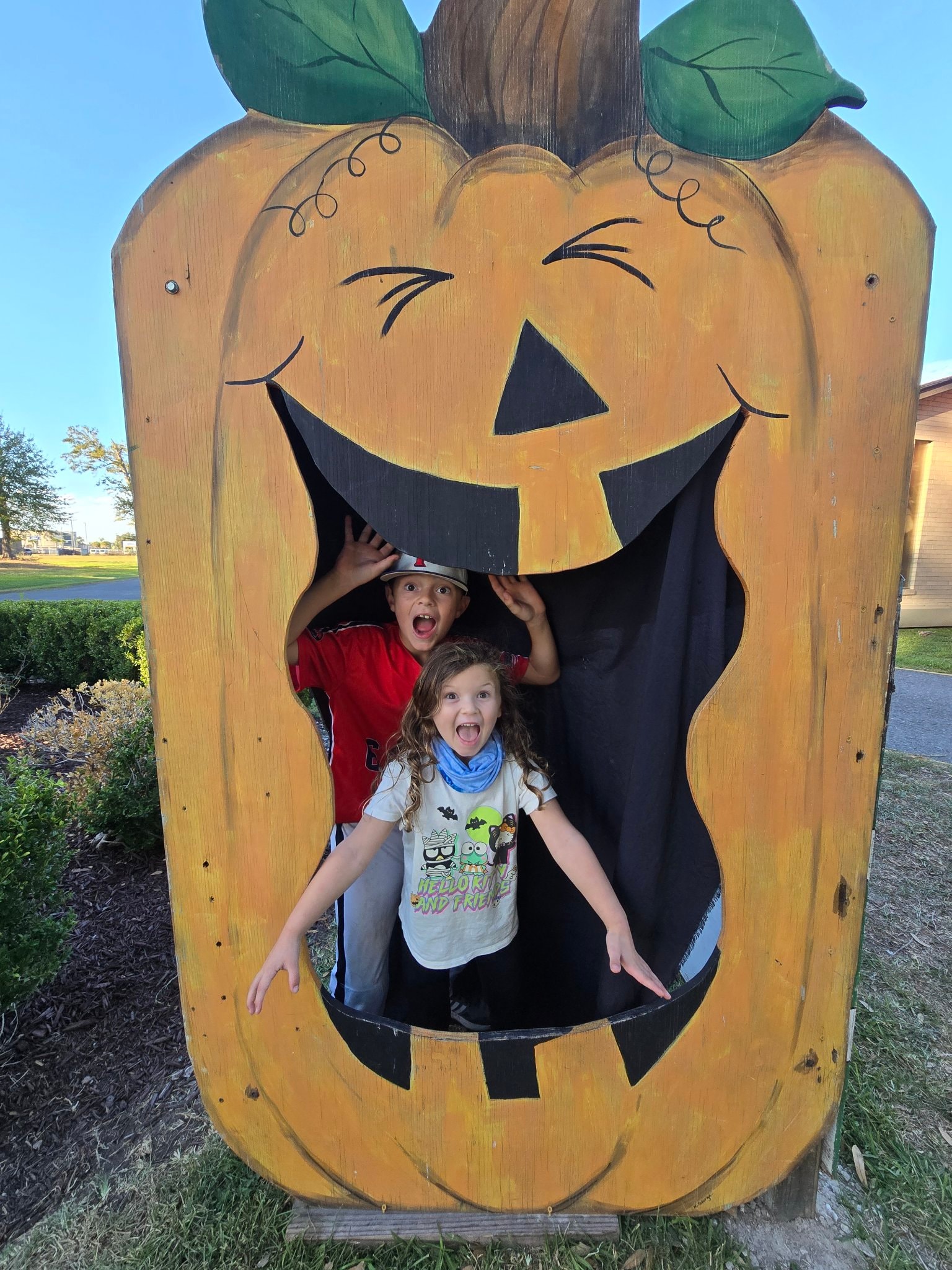 Kids peeking through a giant wooden pumpkin face cutout