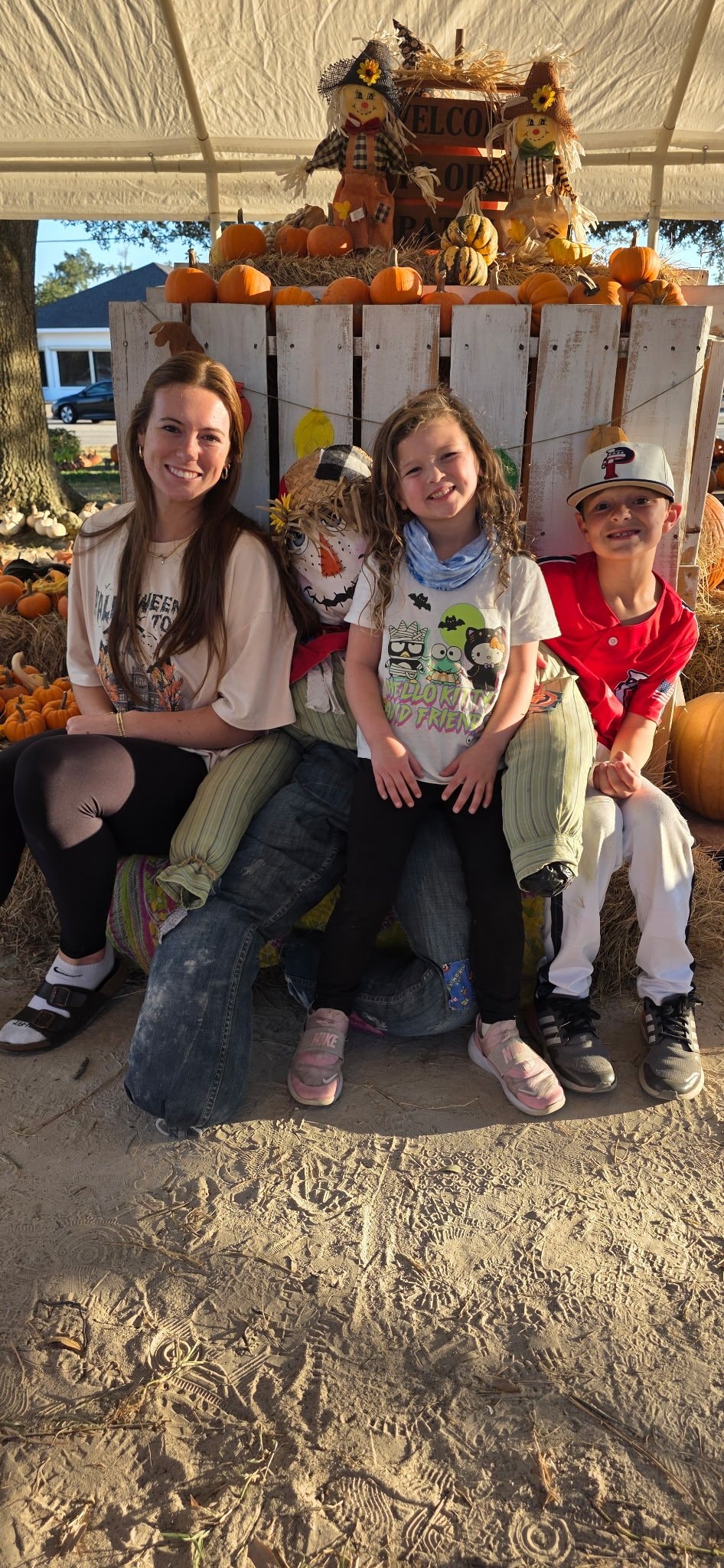 Family sitting on a hay bale bench with scarecrow decorations at the pumpkin patch