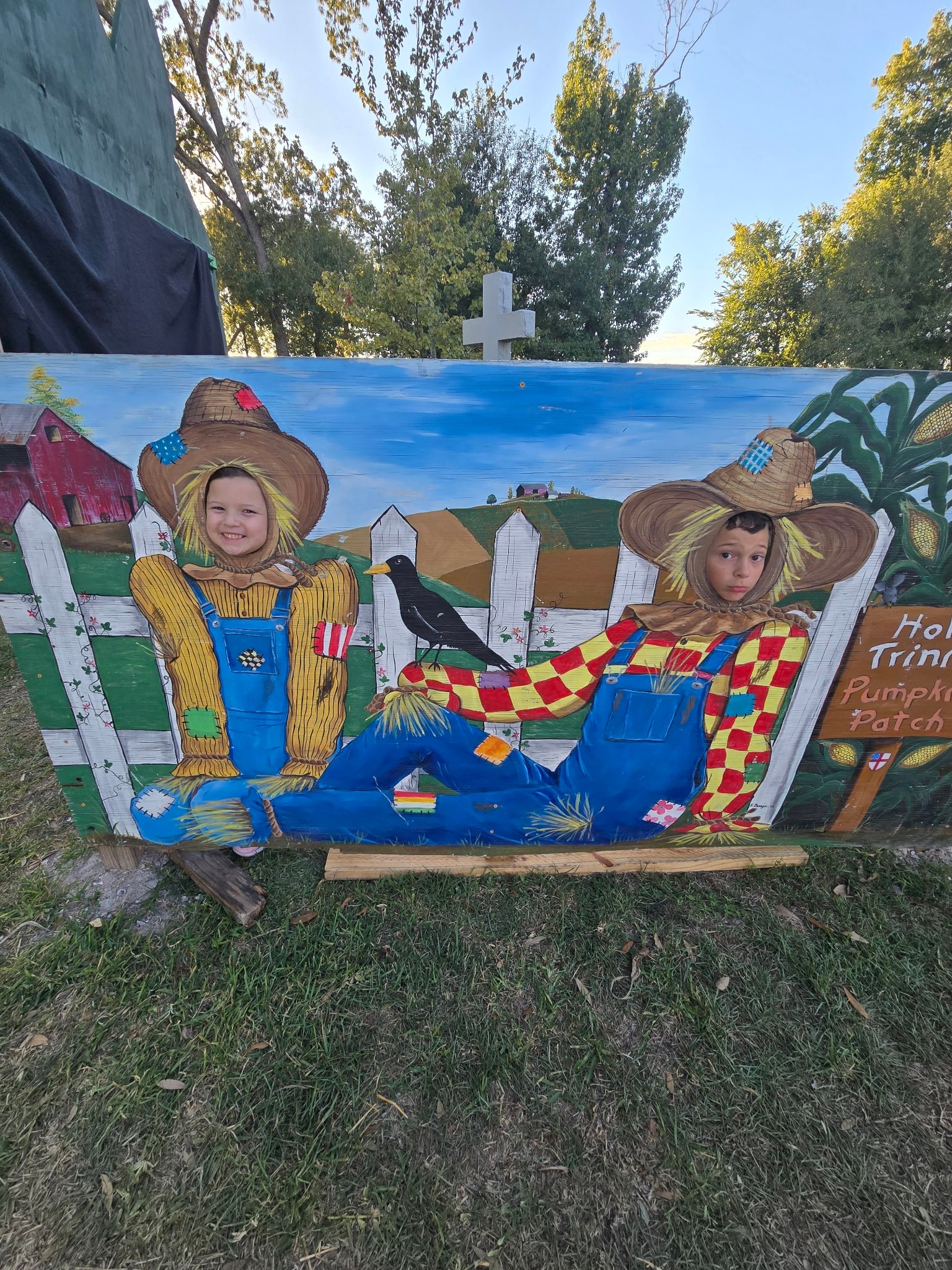Kids posing as scarecrows in a painted cutout board at the pumpkin patch